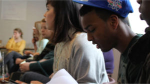 Two young people in a workshop, one wearing a cap looking down at some paper